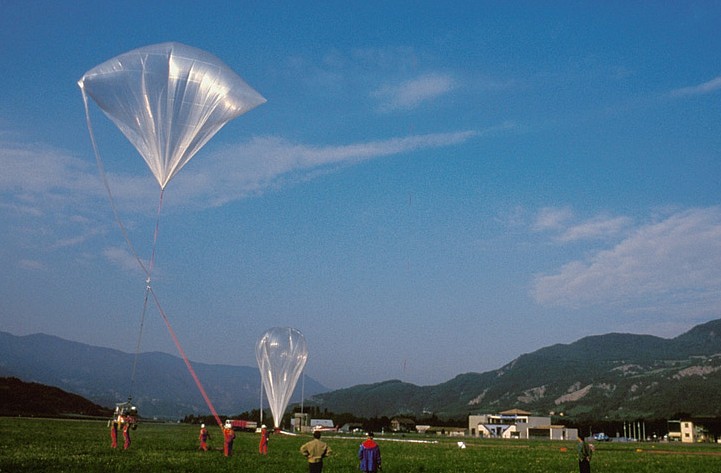 In the background the main balloon fully inflated. At left in the foreground a tetraedral auxiliary balloon holds the gondola.